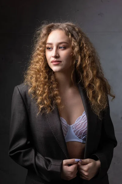 Stüdyoda uzun saçlı, ceketli, kızıl saçlı, kıvırcık bir kızın portresi. Kıvrımlı göğüslerini sütyen içinde gösteriyor..