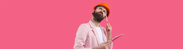 年轻的建筑工程师头戴橙色硬礼帽 穿着粉色夹克 站在红色工作室的背景 一个手里拿着石碑的人 — 图库照片