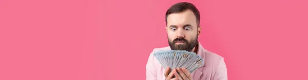 一个心满意足的年轻商人的画像 他身穿粉色夹克 留着胡子 向我们展示在红色工作室背景下的美元钞票 尝起来像钱的味道 — 图库照片