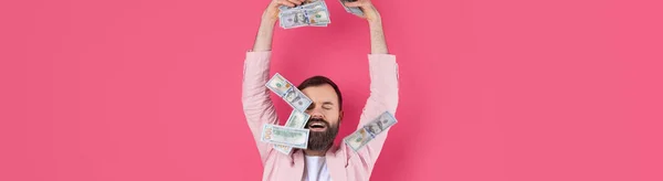ピンクのジャケットを着た髭を生やした若いビジネスマンの肖像画は 赤いスタジオの背景に 紙幣を示しています お金の匂い — ストック写真