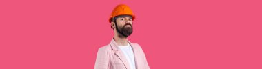 Genç inşaat mühendisinin portresi kırmızı stüdyo arka planında duran pembe ceketli turuncu bir şapka giyer..