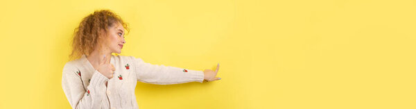 Молодая девушка с кудрявыми волосами с жестом на фоне студии.