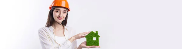 一个戴着建筑头盔的年轻女建筑师展示了一座绿色房子的模型 出售生态不动产 — 图库照片
