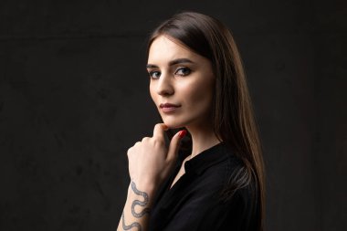 Stüdyoda uzun saçlı genç bir esmerin portresi. Koyu renkli dramatik bir fotoğraf. Kolunda yılan dövmesi olan bir kız..