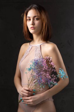 Zarif, çıplak bir beden giymiş güzel seksi bir bayan elinde çiçekler tutuyor. Moda mankeni kızın güzel portresi stüdyoda..