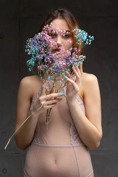 Zarif, çıplak bir beden giymiş güzel seksi bir bayan elinde çiçekler tutuyor. Moda mankeni kızın güzel portresi stüdyoda..