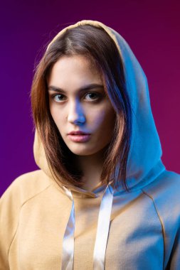 Kapüşonlu bir kadının portresi. Stüdyoda mor bir arka planda güzel bir makyajı var..