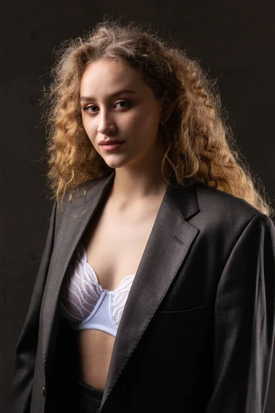 Stüdyoda uzun saçlı, ceketli, kızıl saçlı, kıvırcık bir kızın portresi. Kıvrımlı göğüslerini sütyen içinde gösteriyor..