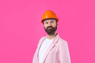 Genç inşaat mühendisinin portresi kırmızı stüdyo arka planında duran pembe ceketli turuncu bir şapka giyer..