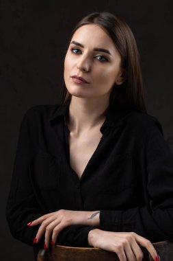 Stüdyoda uzun saçlı genç bir esmerin portresi. Koyu renkli dramatik bir fotoğraf. Kolunda yılan dövmesi olan bir kız..