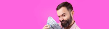 Pembe ceketli sakallı, mutlu genç bir iş adamının portresi kırmızı bir stüdyonun arka planında bize dolar banknotları gösteriyor. Tat, para kokusu..