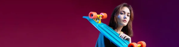 若いです美しいですファッショナブルなヒップスター女の子身に着けていますAスケートボードで彼女の手に紫色のスタジオの背景 — ストック写真