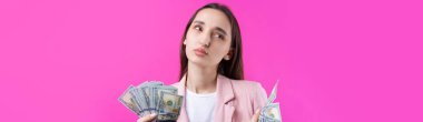 Pembe ceketli bir kadın dolar banknotları tutar, kafası karışmış bir iş kızı kırmızı arka planda dolar saklar..