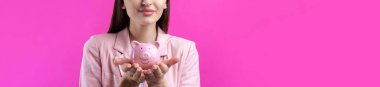 Pembe ceketli şirin bir kız elinde 3 boyutlu bir kumbara tutuyor. Stüdyoda pembe üzerine yakın plan güzel bir portre.