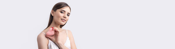 Beautiful smiling woman with clean skin, natural make-up and white teeth on a gray background. Holding a pink hygienic heart.