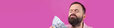 Pembe ceketli sakallı, mutlu genç bir iş adamının portresi kırmızı bir stüdyonun arka planında bize dolar banknotları gösteriyor. Tat, para kokusu..
