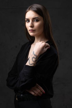 Stüdyoda uzun saçlı genç bir esmerin portresi. Koyu renkli dramatik bir fotoğraf. Kolunda yılan dövmesi olan bir kız..