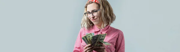 灰色の背景の上に米ドルのお金を持つメガネの赤いチェックのシャツを着た若い美しい女性のクローズアップ — ストック写真