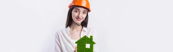 一个戴着建筑头盔的年轻女建筑师展示了一座绿色房子的模型 出售生态不动产 — 图库照片