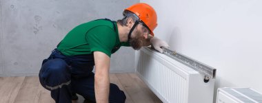 Erkek bir tesisatçı bir apartmanın ısıtma sistemine radyatör yerleştiriyor. Tulumlu ve ingiliz anahtarı olan bir adam..