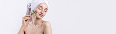Kalın kaşlı güzel bir kız, beyaz arka planda mükemmel bir ten, kafasında havlu, güzel bir fotoğraf. Kozmetik rulo tutuyor..