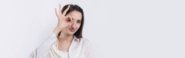 Close up portrait of attractive quirky young woman making binoculars with hands showing ok gesture on white studio background.
