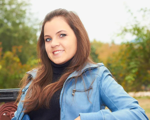 Aantrekkelijke lachende meisje in een blauwe jas zittend op een bankje — Stockfoto