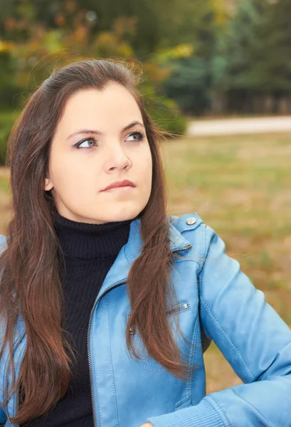Attractive young girl in a blue jacket, sitting on a bench in th — Stock Photo, Image