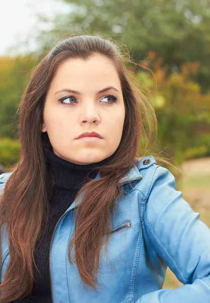 Attractive young girl in a blue jacket, sitting on a bench in th — Stock Photo, Image