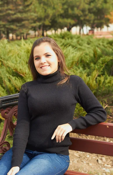 Attraktive junge Frau im schwarzen Pullover sitzt auf einer Parkbank — Stockfoto