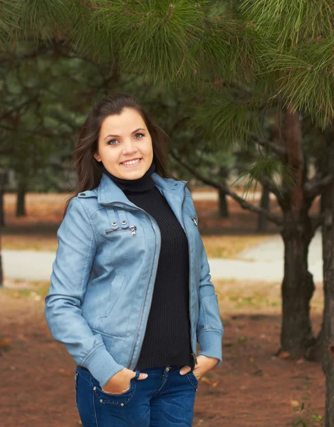Привлекательная улыбающаяся девушка в синей куртке, стоящая под елкой — стоковое фото