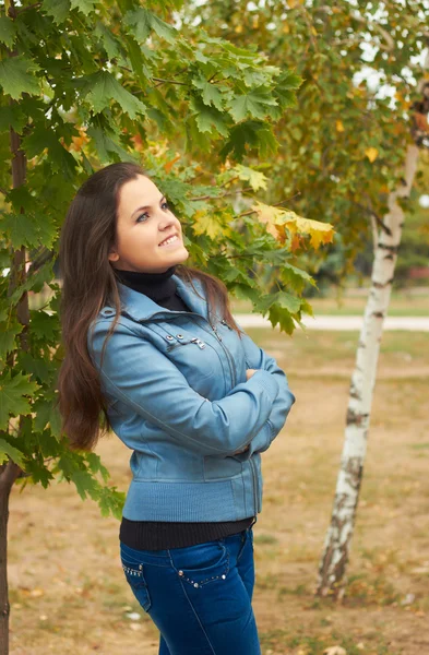 Attraktives lächelndes Mädchen in blauer Jacke, das unter einem Baum in — Stockfoto