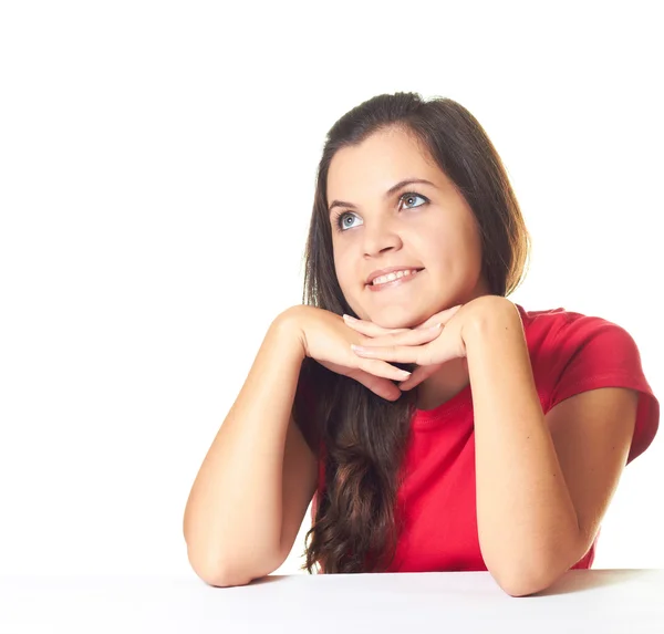 Привлекательная молодая улыбающаяся девушка в красной рубашке сидит за столом — стоковое фото