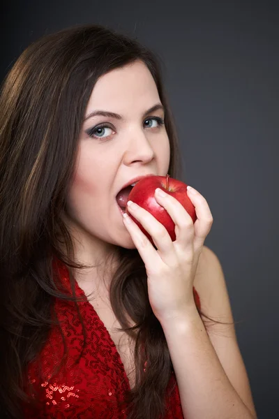 Aantrekkelijke jonge vrouw in een rode jurk. vrouw die een rode appel eten. — Stockfoto