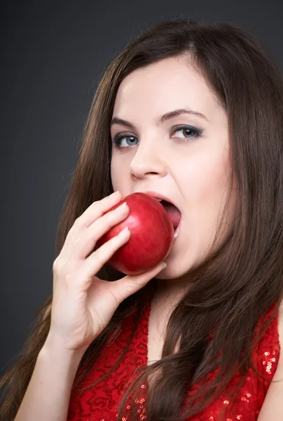 Attraktiv ung kvinna i en röd klänning. kvinna bita ett rött äpple. — Stockfoto