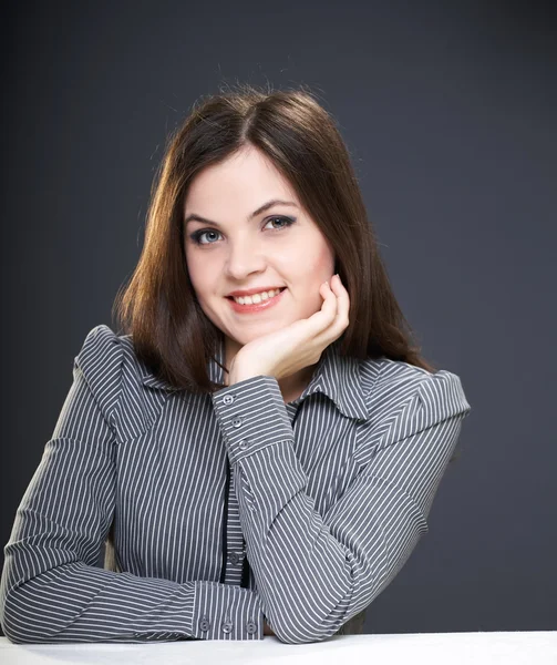 Mujer joven feliz en una blusa gris sentada a la mesa . — Foto de Stock