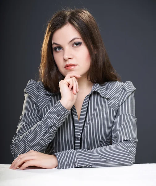 Jovem atraente em uma blusa cinza sentada à mesa . — Fotografia de Stock