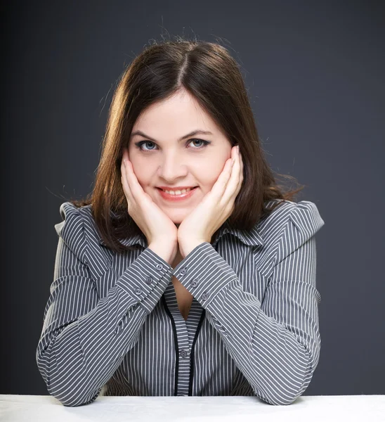 Attraente giovane donna in una camicetta grigia seduta a tavola . — Foto Stock