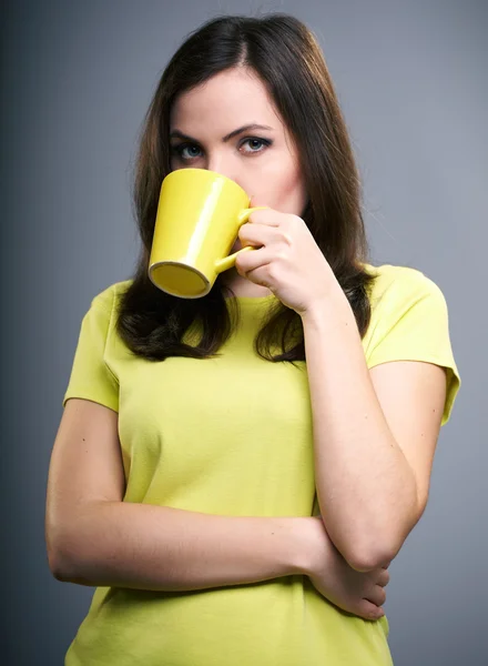 Привлекательная молодая женщина в жёлтой рубашке. Женщина пьет из — стоковое фото