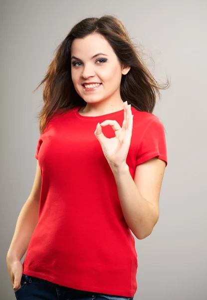 Aantrekkelijke jonge vrouw in een rode shirt. vrouw toont een teken oke. — Stockfoto