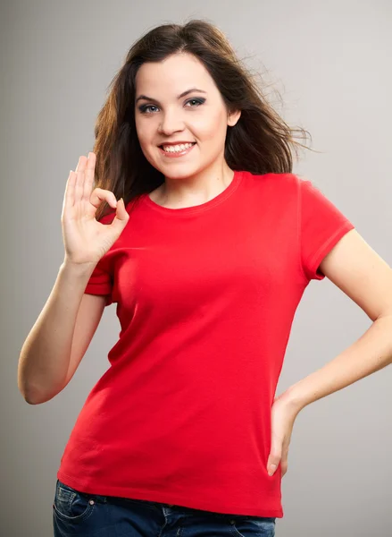 Aantrekkelijke jonge vrouw in een rode shirt. vrouw toont een teken oke. — Stockfoto