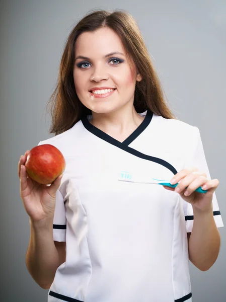 Attractive young nurse. Woman holding a toothbrush and red appl — Stock Photo, Image