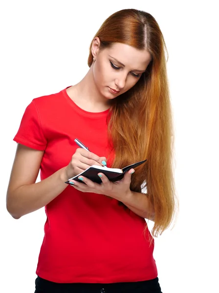 Attractive young woman in a red shirt. Writes in a notebook. — Stock Photo, Image