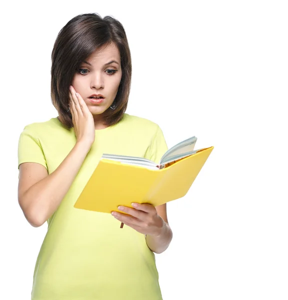 Meglepett, fiatal nő, egy sárga pólót. egy sárga könyvet olvas. — Stock Fotó