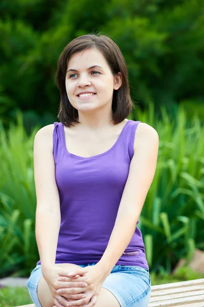 Attractive young woman in a lilac shirt. Sitting on a bench in a Stock Image