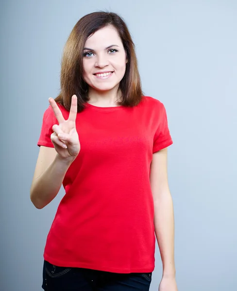 Gelukkig jonge vrouw in een rode shirt. geeft een symbool van de overwinning. — Stockfoto