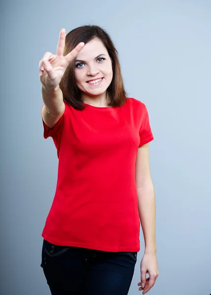 Lächelnde junge Frau im roten Hemd. zeigt ein Symbol des Sieges. — Stockfoto