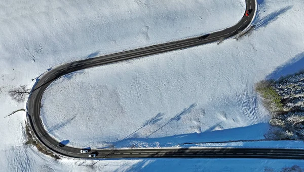 Karlı arazinin hava aracı görüntüsü. Kavisli yol ve arabalar.