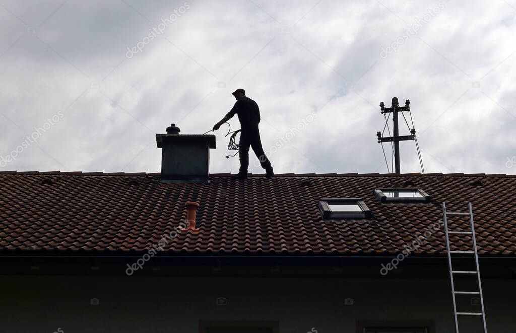 A chimney sweep cleans the chimney on a house roof