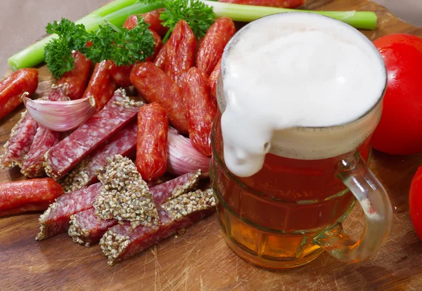 Mug of beer and an assortment of salami and vegetables on a cutt — Stock Photo, Image